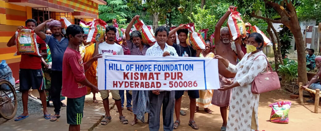 A group of people in West Bengal with ration sacks on their shoulders, holding a banner reading “Hill of Hope Foundation, Kismatpur, Hyderabad - 500086”.