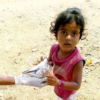 A photograph of a young girl being handed a meal pack.