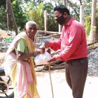 A photograph of an elderly woman being given a meal pack by a volunteer.