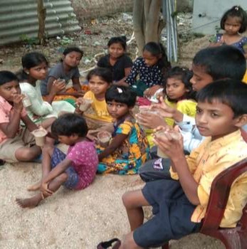 A photograph of a dozen children seated, holding and drinking their nutrition drink.