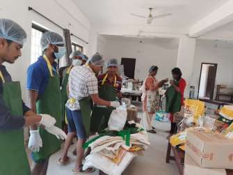 A photograph of eight people wearing various personal protective equipment, working together to pack ration kits.