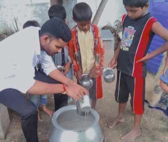 A photograph of a volunteer pouring the nutrition drink into a cup; several children are watching and waiting for their turn.